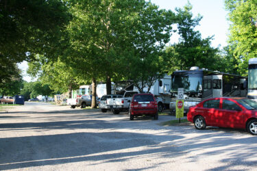 RVs and Cars Parked on a Gravel Road Lined with Trees in a Campground. A Speed Limit Sign is Visible in the Foreground at Council Road RV Park